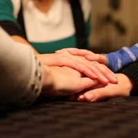 Nuoria ja vanhoaja käsiä päällekkäin pöydällä