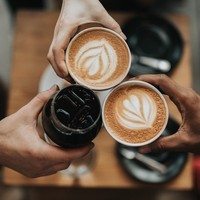 Kolme kättä, jotka kaksi pitelee kahvimukia missä kahvia