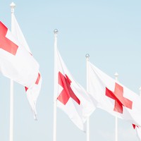 Rivi liehuvia lippuja lipputangoissa, punainen risti valkoisella pohjalla
